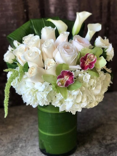 Cream, white, and green flowers arranged in a tall glass vase