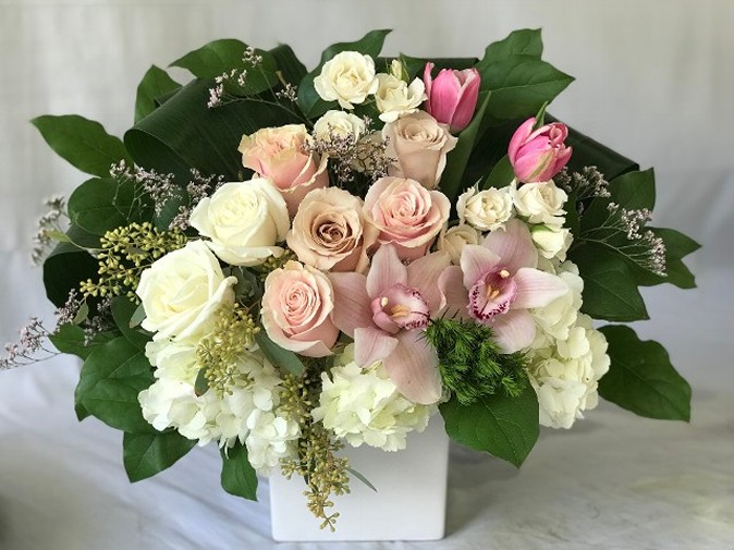 Mothers Day arrangement with 10 premium blooms consisting of tulips, roses, orchids and hydrangea. Colors and flowers may vary slightly. Front facing arrangement in a white ceramic container or wood box depending upon dollar amount. 